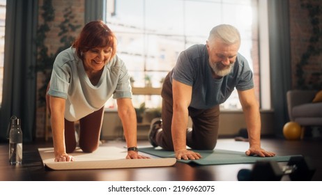 Happy Middle Aged Couple Doing Gymnastics And Yoga Stretching Exercises Together At Home On Bright Morning. Senior Man And Woman Motivate Each Other To Be Healty. Lifestyle And Fitness Concept.