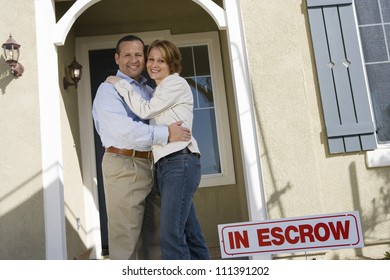 Happy Middle Aged Couple Embracing In Front Of House For Sale