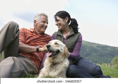 Happy Middle Aged Couple And Golden Retriever Relaxing On Grass