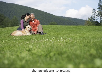 Happy Middle Aged Couple And Golden Retriever Relaxing On Grass