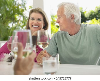 Happy Middle Aged Couple Having Wine With Friend At Verandah Table