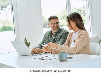 Happy middle aged couple older mature man and woman using laptop computer holding credit card buying online, making banking payments, doing ecommerce shopping on website sitting at home table. - Powered by Shutterstock