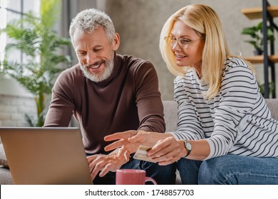 Happy middle aged couple on sofa websurfing and shopping on internet at home