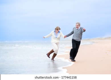 Happy middle aged couple running on a beach holding hands and jumping away from the waves - Powered by Shutterstock