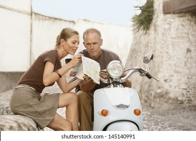 Happy middle aged couple with scooter reading map in Granada; Spain - Powered by Shutterstock