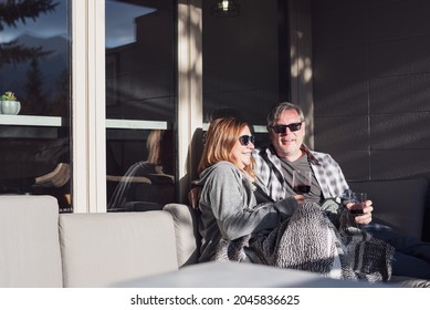 Happy middle aged couple snuggled up in a blanket sitting on a patio couch enjoying wine - Powered by Shutterstock