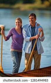 Happy Middle Aged Couple Standing With Their Canoe Near A Lake.