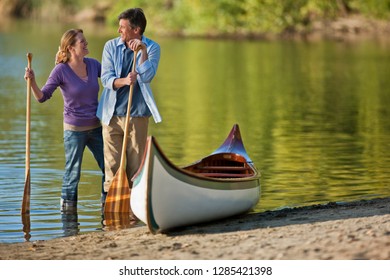 Happy middle aged couple standing with their canoe near a lake.