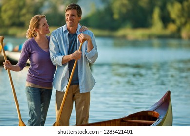 Happy Middle Aged Couple Standing With Their Canoe Near A Lake.