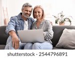 Happy middle aged couple using laptop on sofa at home