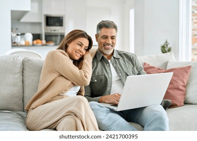 Happy middle aged couple using laptop relaxing on couch at home. Smiling mature man and woman looking at computer watching video, browsing or shopping in ecommerce store sitting on sofa in living room - Powered by Shutterstock