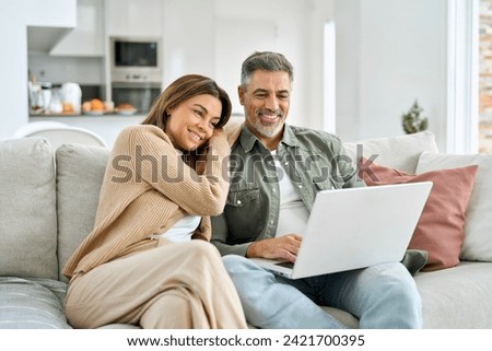 Happy middle aged couple using laptop relaxing on couch at home. Smiling mature man and woman looking at computer watching video, browsing or shopping in ecommerce store sitting on sofa in living room