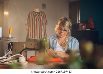 Happy middle aged dressmaker woman sitting and sewing on a sewing machine a in studio. Tailor woman working on clothes in tailoring atelier. Creating new fashionable style. - Shutterstock ID 2167139413