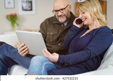 Happy Middle Aged European Couple On Phone With Technical Support As They Smile And Look At Their Open Laptop Computer