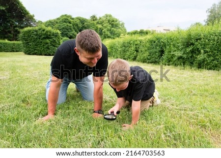 Happy middle aged father playing with his little son in the park. Son holds a magnifying glass and examines the beetle.