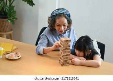 Happy Middle Aged Grandma And Little Grandchild Playing Wood Block Stacking Board Game Together In Living Room. Multi Generational And Family Concept