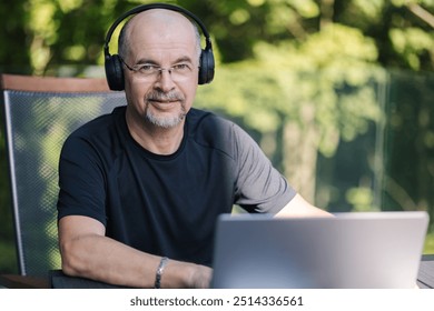 Happy middle aged male freelancer in headphones looking at laptop and work - Powered by Shutterstock