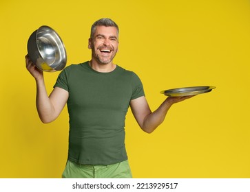 Happy Middle Aged Man Hold Open Empty Metallic Cloche For Mock Up Or Product Placement Isolated On Yellow Background. Romantic Dinner At Home Man Cooking Skills. Service, Restaurant, HoReCa Concept.