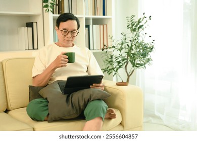 Happy middle aged man sipping coffee from a green mug and browsing on digital tablet - Powered by Shutterstock