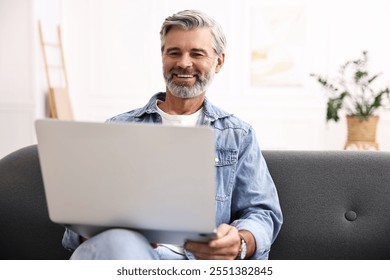 Happy middle aged man using laptop on sofa at home