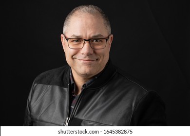 Happy Middle Aged Man Wearing Glasses And Black Jacket On Dark Background