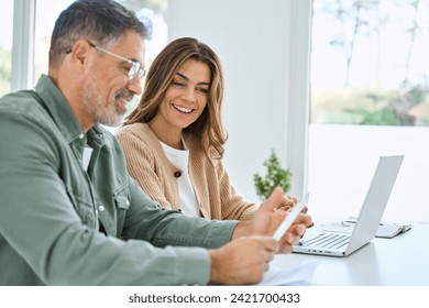 Happy middle aged mature couple using laptop counting taxes refund receipts to save money at home. Old man and woman paying bills online planning financial budget savings calculating payment at table. - Powered by Shutterstock