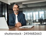 Happy middle aged professional business man, older executive ceo manager, smiling mature entrepreneur wearing glasses and shirt sitting at office desk working on laptop computer. Copy space. Portrait.