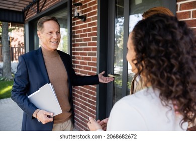 Happy Middle Aged Realtor Pointing At House Near Interracial Lesbian Couple