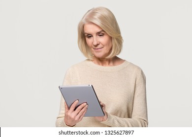 Happy Middle Aged Senior Lady Holding Digital Tablet Reading Online Social Media News, Smiling Mature Old Woman Doing Internet Shopping Using Gadget Pc Isolated On White Grey Studio Background