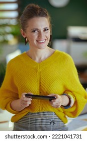 Happy Middle Aged Small Business Owner Woman In Yellow Sweater In The Modern Green Office Using Smartphone.