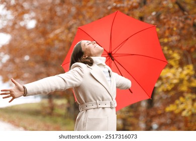 Happy middle aged woman breathing fresh ait and stretching arms celebrating with red umbrella in winter in a forest - Powered by Shutterstock