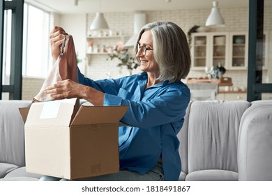 Happy Middle Aged Woman Buyer Opening Parcel Box At Home. Smiling Old Mature Female Customer Shopper Receiving Online Shop Purchase Buying Clothes Unpacking Delivery Postal Shipping Package On Couch.