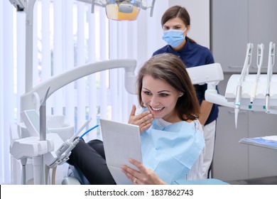 Happy Middle Aged Woman With Doctor Dentist Looking In Mirror At Teeth, Sitting In Dental Chair. Medicine, Dentistry And Health Care Concept