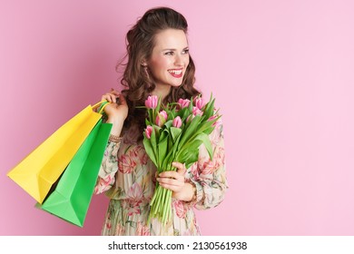 happy middle aged woman in floral dress with tulips bouquet and shopping bags isolated on pink background. - Shutterstock ID 2130561938