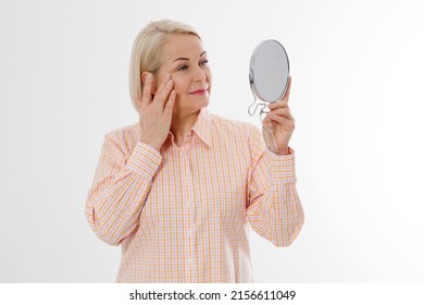 Happy Middle Aged Woman Looking In Mirror On Her Face With Wrinkles On The Forehead And Wrinkle Skin. Collagen And Face Injections Concept. Menopause. Copy Space And Mock Up.