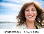 Happy middle aged woman with messy hair laughing on the beach