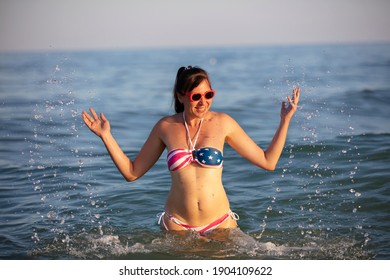 Happy middle aged woman splashing sea water in swimsuit with American flag print. - Powered by Shutterstock