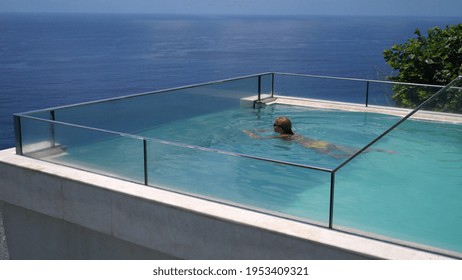 Happy Middle Aged Woman Swimming In An Infinity Pool Overlooking An Ocean. Luxurious Resorts Concept.