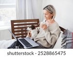 Happy middle aged woman using her laptop on the sofa at cozy home