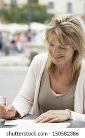 Happy Middle Aged Woman Writing Letter At Outdoors Cafe