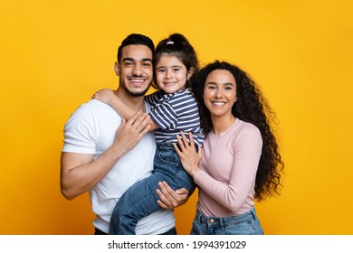 Happy Middle Easter Family Of Three With Little Daughter Embracing And Smiling At Camera, Loving Arab Parents And Cute Female Child Posing Togethet Over Yellow Studio Backgriund, Free Space