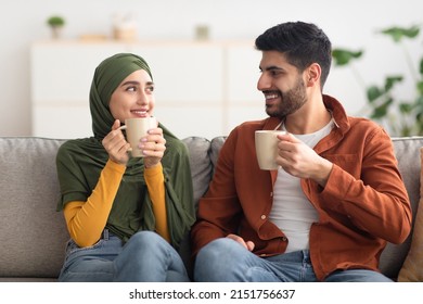 Happy Middle Eastern Couple Having Coffee Holding Cups Sitting On Sofa Talking Having Date At Home. Family And Marriage Lifestyle, Romantic Relationship Concept