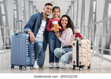 Happy Middle Eastern Family Of Three Posing In Airport Terminal, Cheerful Arab Parents And Their Cute Little Daughter Holding Suitcases, Passports And Tickets And Smiling At Camera, Ready For Travel