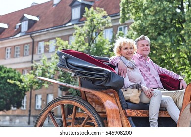 Happy middle-aged couple sitting in horse cart on city street