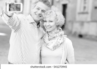 Happy Middle-aged Couple Taking Selfie Through Smart Phone In City