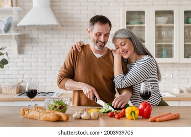 Happy middle-aged family cooking vegetable salad in the kitchen at home together. Mature wife helping prepare food meal her husband. Vegetarian healthy eating - Powered by Shutterstock