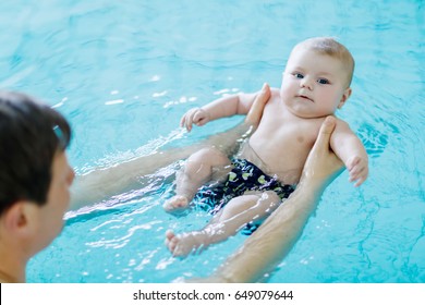 Happy middle-aged father swimming with cute adorable baby in swimming pool. Smiling dad and little child, newborn girl having fun together. Active family spending leisure and time in spa hotel.