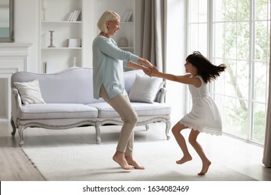 Happy middle-aged grandmother play dancing and swirling in living room with cute little granddaughter, energetic senior granny have fun engaged in childish funny activity with small preschooler child - Powered by Shutterstock