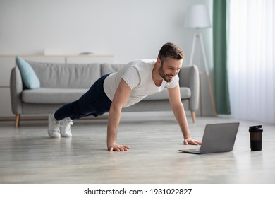 Happy middle-aged man in sportswear doing push-ups, using laptop, having online fitness class from home, living room interior, copy space. Sporty bearded man enjoying daily training, watching video - Shutterstock ID 1931022827