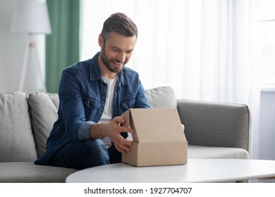Happy middle-aged man unpacking delivery box, sitting on couch by tea table, home interior. Satisfied customer cheerful man opening package, ordering clothes or gadgets on Internet, copy space - Powered by Shutterstock